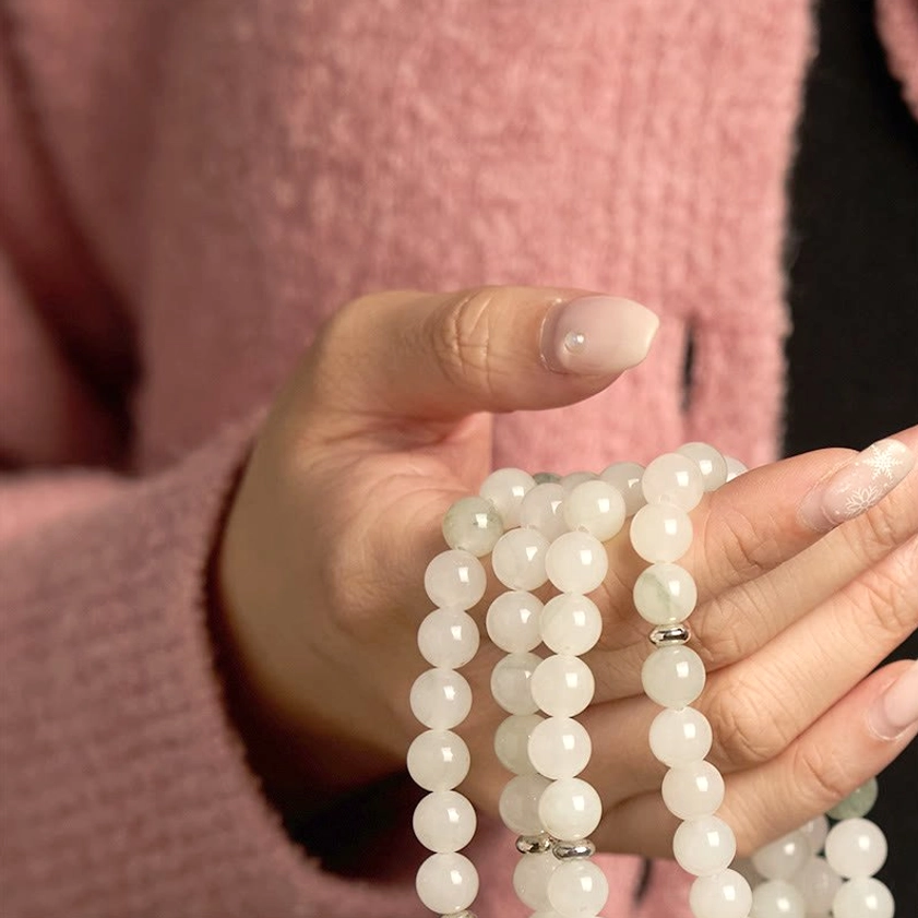 Hands holding white and green jade mala beads, showcasing natural stone texture and spiritual craftsmanship