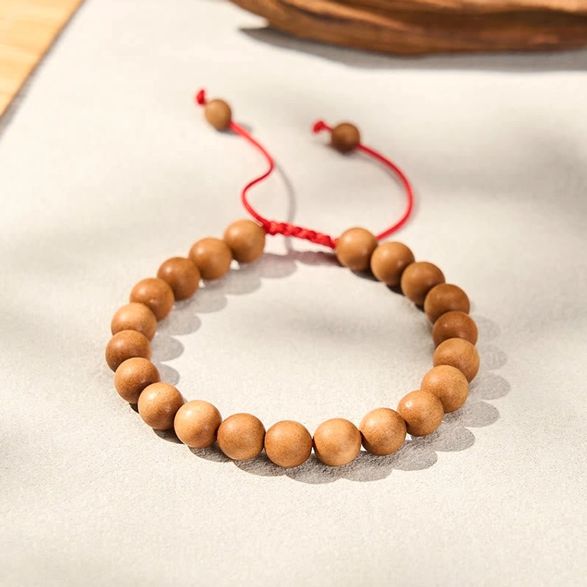 Handcrafted sandalwood mala bracelet with uniform tan beads and red silk cord with small end beads on light paper background