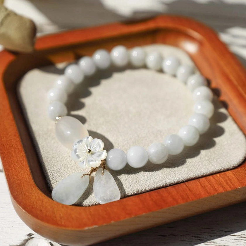 Buddhist white jade luck bracelet with teardrop jade charms on wooden tray with velvet pad top-down view