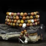 Natural wood 108 bead Buddhist mala prayer beads with silver metal pendants on weathered wooden surface, close-up side view