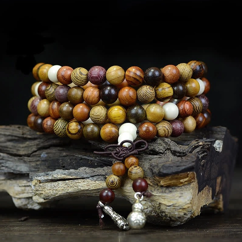 Natural wood 108 bead Buddhist mala prayer beads with silver metal pendants on weathered wooden surface, close-up side view