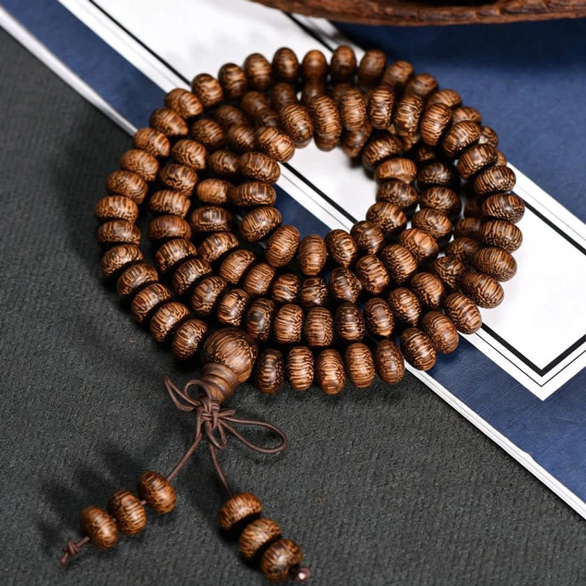 Coiled wood bead mala with knotted tassel on dark background with blue stationery props