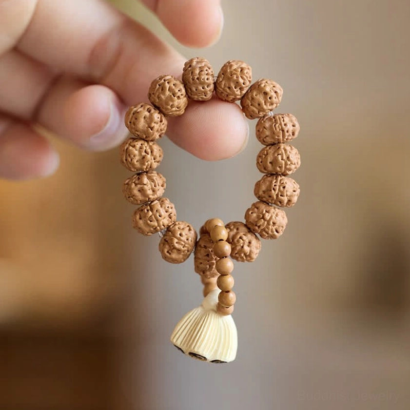 Close-up fingers holding natural wood meditation bracelet with large carved lotus pod pendant showing craftsmanship detail