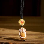 Nine-eye dzi bead agate pendant necklace with gold decorative cap and red agate accent stone on wooden surface