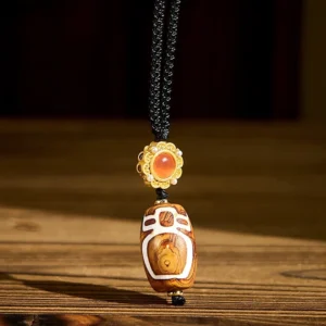 Nine-eye dzi bead agate pendant necklace with gold decorative cap and red agate accent stone on wooden surface