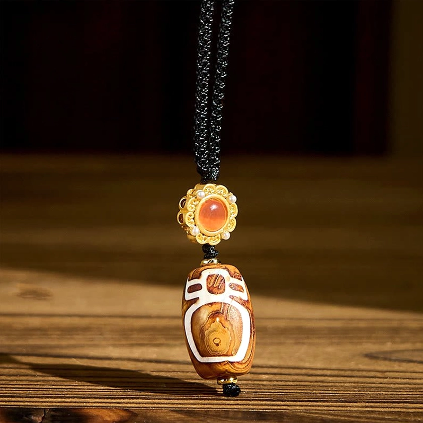 Nine-eye dzi bead agate pendant necklace with gold decorative cap and red agate accent stone on wooden surface