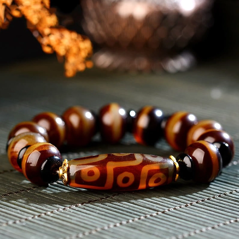 Nine-eye dzi bead agate bracelet for wealth and protection displayed on bamboo mat with dried flowers and gold spacer accents