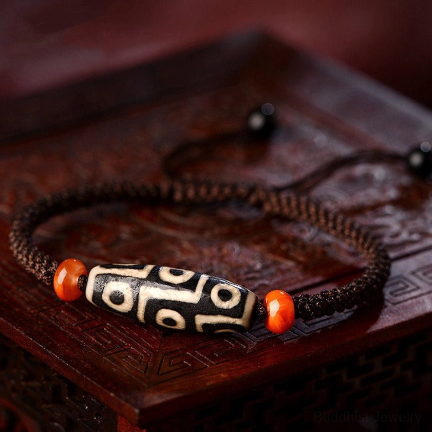 Classic Nine-Eye Dzi Bead bracelet with adjustable braided rope on carved wooden tabletop