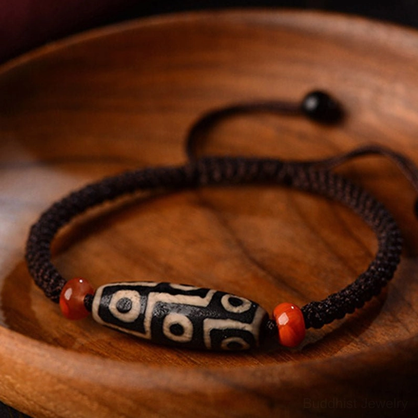 Black and white Nine-Eye Dzi Bead with red agate spacers on dark blurred background highlighting stone details