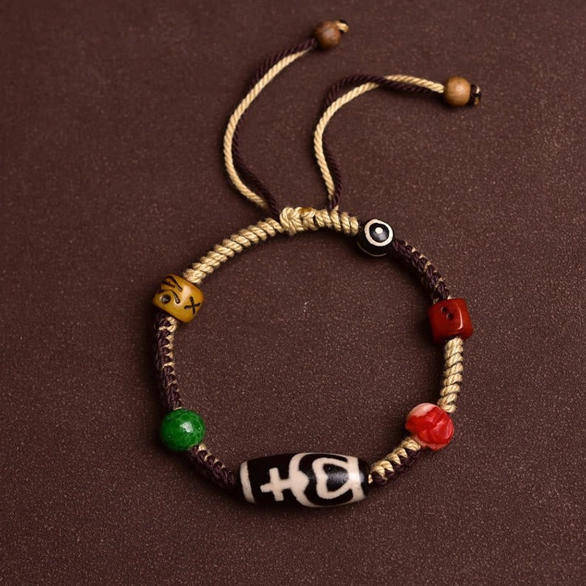 Top-down flat lay of nine-eye dzi bead Buddhist bracelet showing dual-color woven cord, hand-painted dzi bead, and wooden accent beads