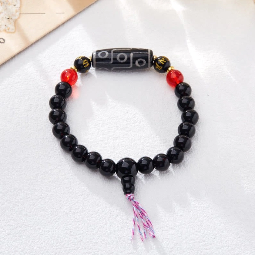 Buddhist nine-eye Dzi bead bracelet flat lay displaying black onyx beads, red accent beads, metal mantras, and pink tassel clasp