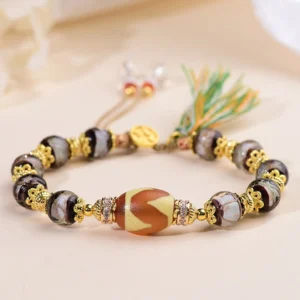 Nine-eye dzi bead liuli glass bracelet with gold metal spacers and tassel pendant, oblique view on light background