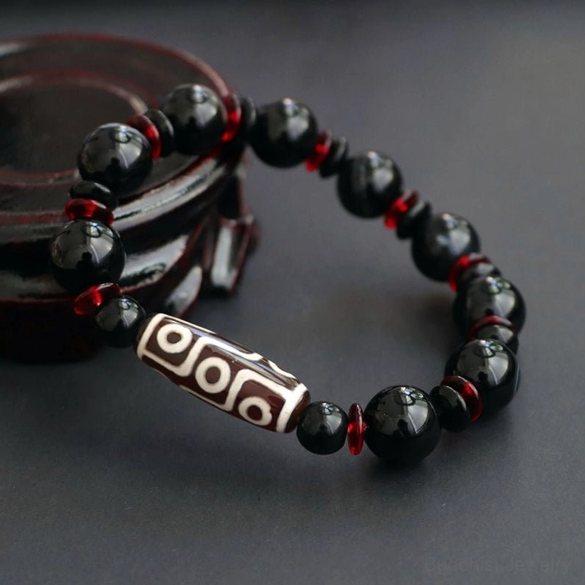 Nine-Eye Dzi Bead Bracelet low frontal view on wooden stand with red accents