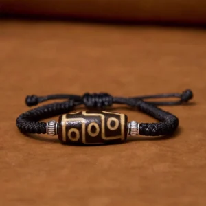 Nine-eye dzi bead bracelet flat lay view showing complete black braided rope with silver metal spacers and hand-painted nine-eye pattern