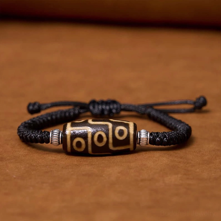 Nine-eye dzi bead bracelet flat lay view showing complete black braided rope with silver metal spacers and hand-painted nine-eye pattern