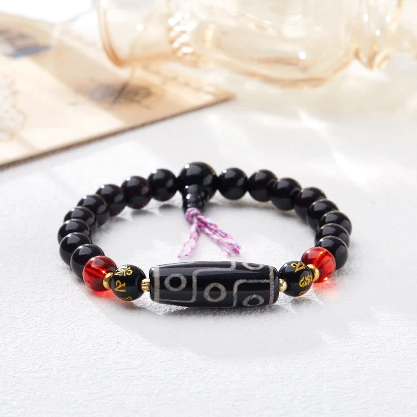 Dzi bead bracelet close-up detail showing Om Mani Padme Hum metal spacers, black onyx beads, and red accent beads
