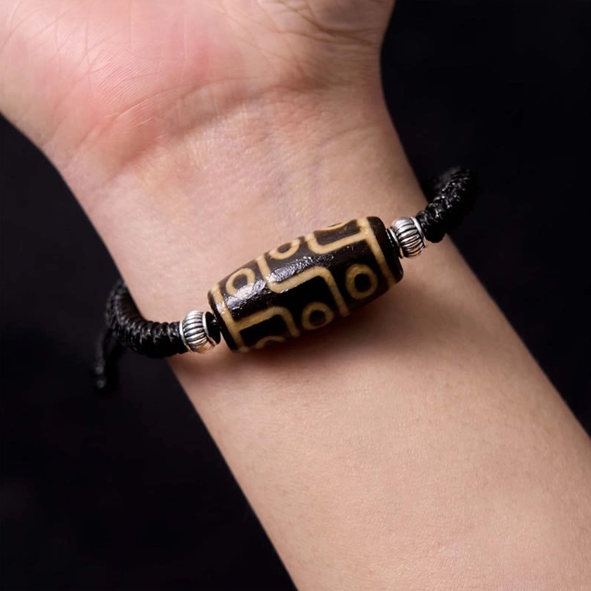 Nine-eye dzi bead bracelet worn on human wrist against dark background demonstrating comfortable fit and real-life wear