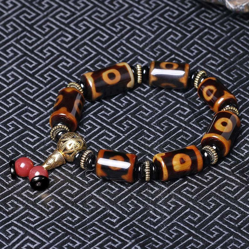 Nine-eye dzi bead bracelet overhead view on black geometric pattern, displaying classic eye patterns and gold-tone metal hardware