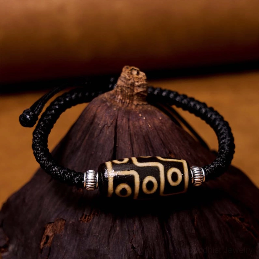 Nine-eye dzi bead bracelet overhead view with textured natural background showing symmetrical design