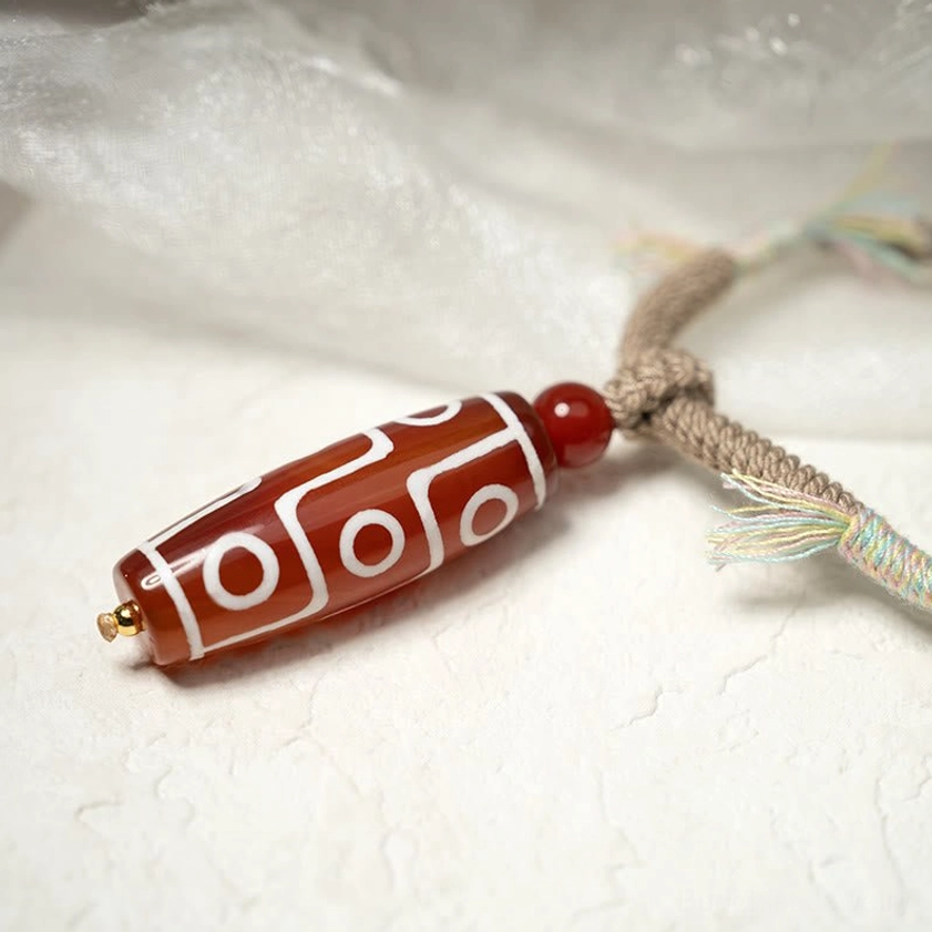 Nine-eye dzi bead bracelet angled view with colorful frayed rope accents and red spacer bead, wearable spiritual protection tool