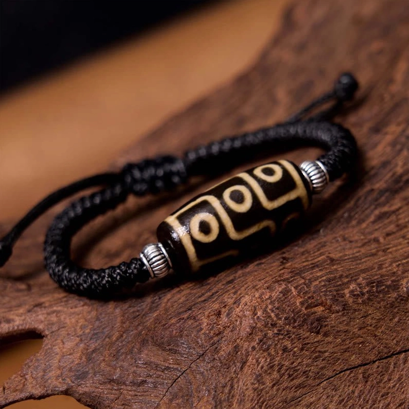 Nine-eye dzi bead bracelet side angle view on dark wooden background displaying detailed nine-eye motif and silver decorative accents