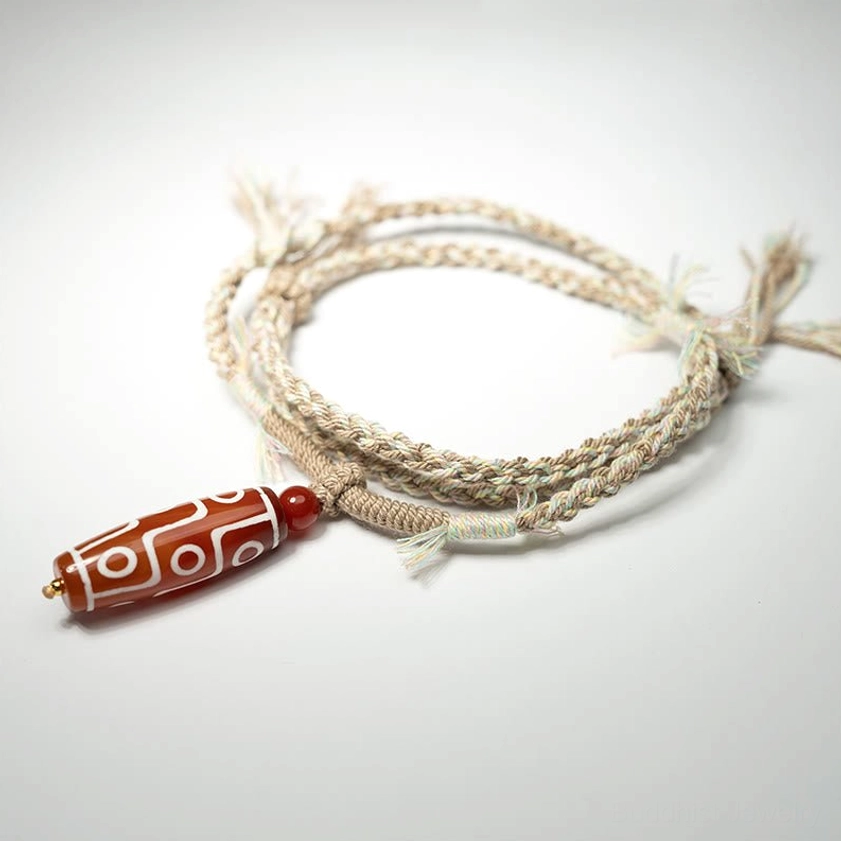 Nine-eye dzi bead wrap bracelet close-up showing coiled hemp rope and red agate spacer bead, authentic buddhist protective jewelry