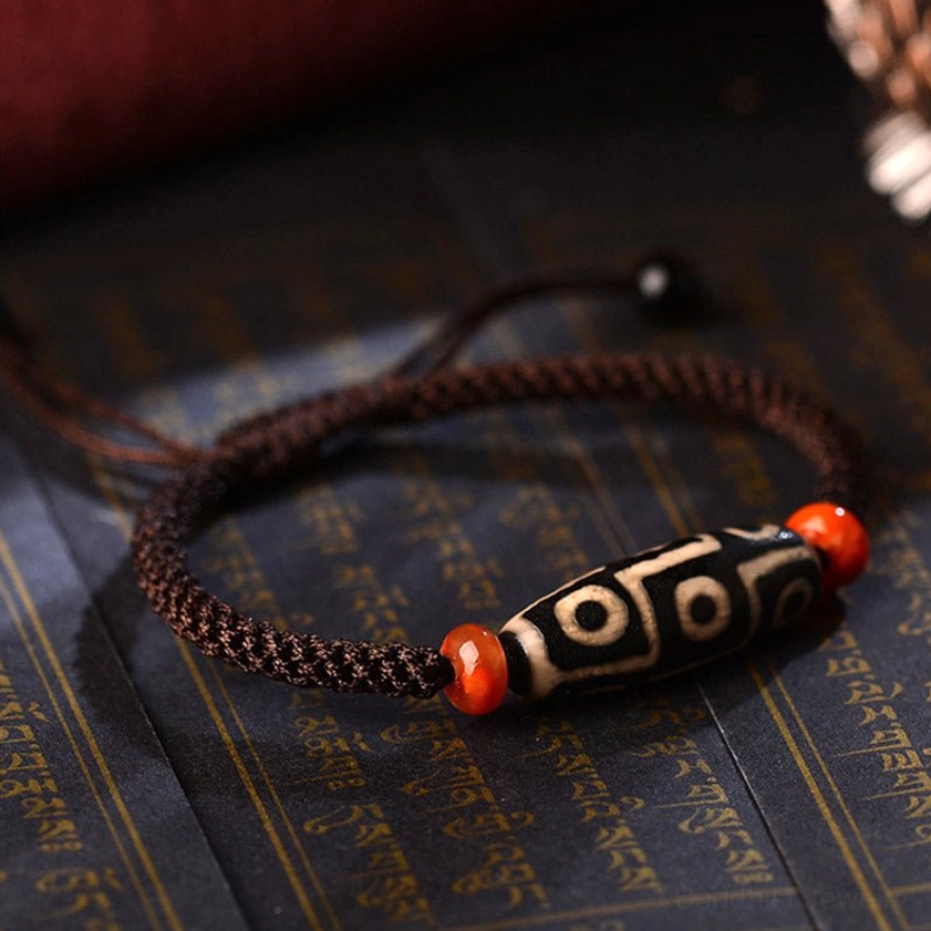 Tibetan Buddhist protection bracelet with black base white dzi patterns and red agate spacers on scripture background