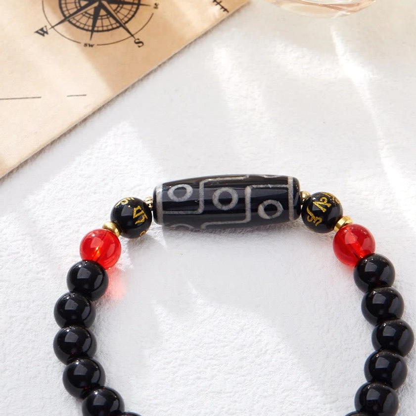 Nine-eye Dzi bead black onyx bracelet angled close-up on vintage map background with engraved sacred symbols visible