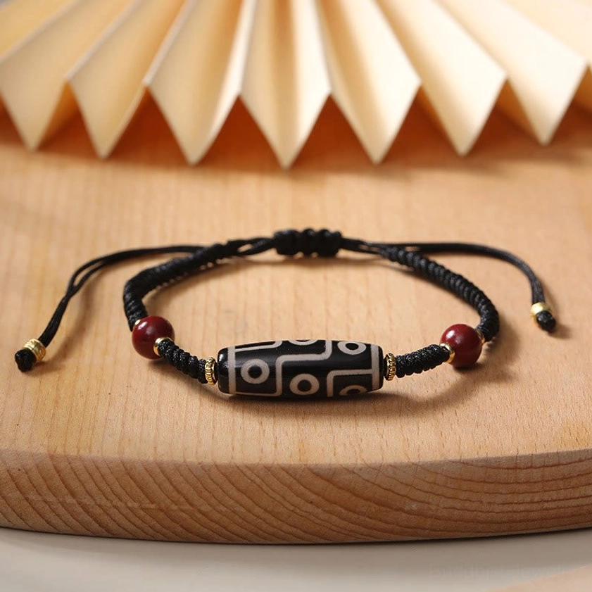 Buddhist nine-eye Dzi bead bracelet featuring black braided cord and gold hardware on vintage paper backdrop