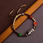 Handmade nine-eye dzi bead braided rope bracelet with black-white patterned bead and colorful accent beads, side view on wooden background
