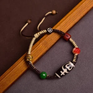 Handmade nine-eye dzi bead braided rope bracelet with black-white patterned bead and colorful accent beads, side view on wooden background