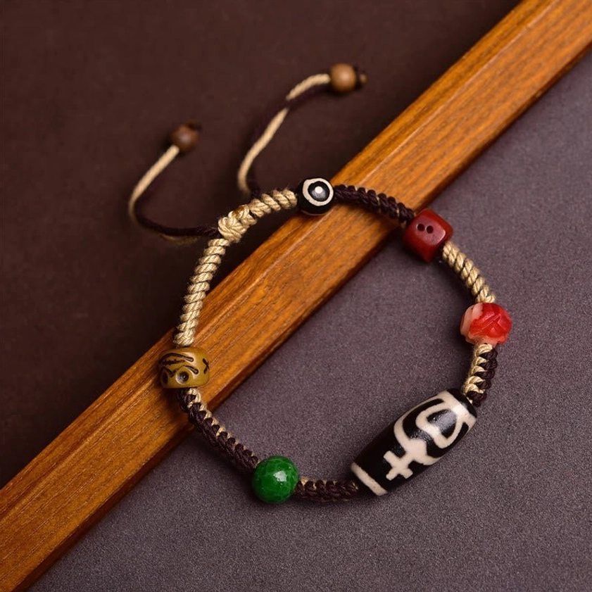 Handmade nine-eye dzi bead braided rope bracelet with black-white patterned bead and colorful accent beads, side view on wooden background