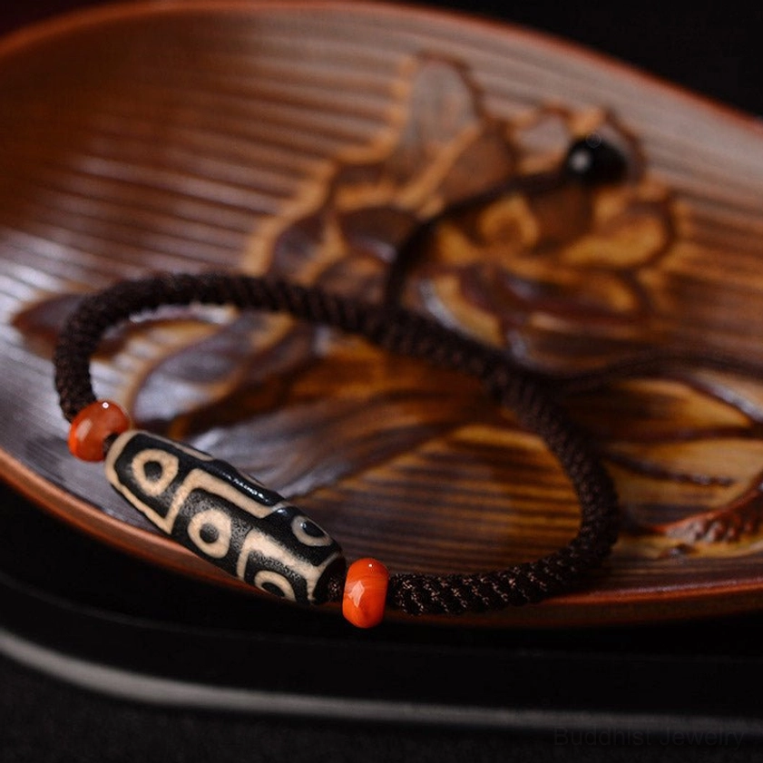 Black and white Nine-Eye Dzi Bead with red agate spacers on carved wooden tray showing adjustable drawstring design