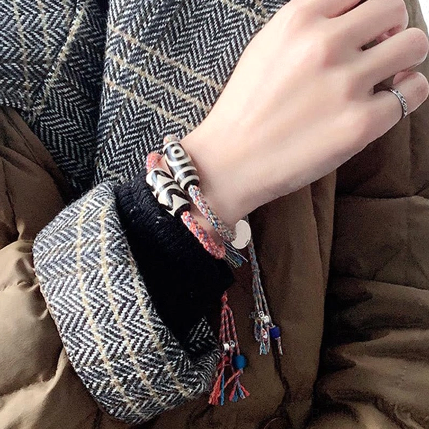 Nine-Eye Dzi Bead Sterling Silver protection bracelet worn on wrist with black-white dzi bead, silver charm, and colorful tassel pendant