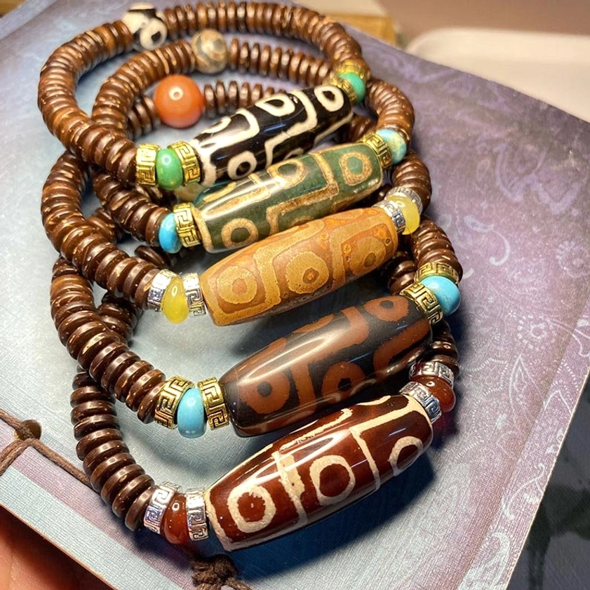 multiple nine-eye dzi bead bracelets displayed together showing diverse color options from black to brown to green with natural gemstone details