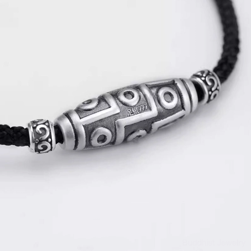 Close-up side view of 999 sterling silver dzi bead pendant showing hallmark and detailed carved nine-eye design