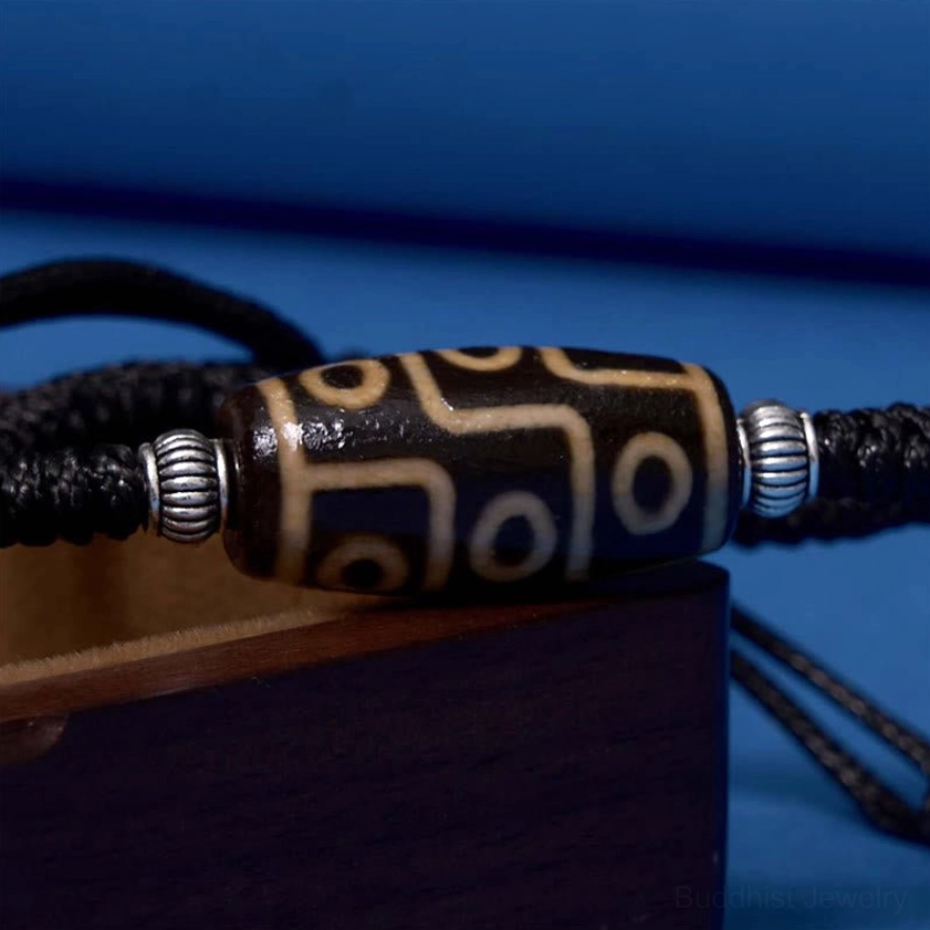 Close-up of nine-eye dzi bead showing detailed hand-painted eye pattern with silver metal spacers on black cord
