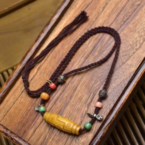 Nine-eye dzi bead copper necklace with colorful mixed beads on wooden tray, featuring traditional braided cord and silver metal accents