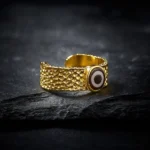 Nine-eye dzi bead adjustable copper brass ring, open cuff design with hammered texture, front angled view on stone surface