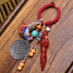 Buddhist Dzi Bead keychain with red braided rope, silver carved Buddha pendant, and colorful tassel on wooden desk