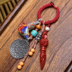 Buddhist Dzi Bead keychain with red braided rope, silver carved Buddha pendant, and colorful tassel on wooden desk