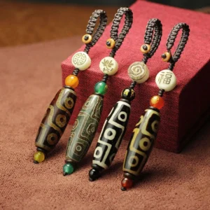 Collection of nine-eye dzi bead keychains in multiple colors including black, red, brown, and green agate showing varied Buddhist patterns displayed on brown cloth with red gift box