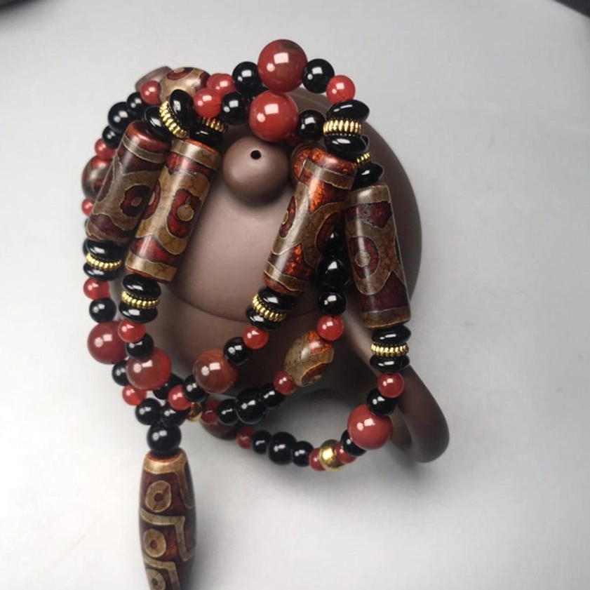 Coiled Nine-Eye Dzi Bead Buddhist necklace close-up on teapot-shaped ceramic holder, highlighting intricate carved patterns with gold accents