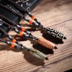 Nine-eye dzi bead necklaces collection in green, black, and brown displayed on wooden table with books and natural decor