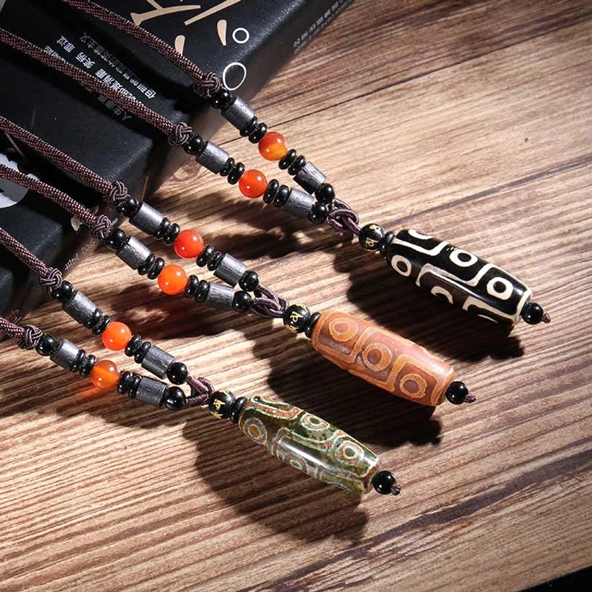 Nine-eye dzi bead necklaces collection in green, black, and brown displayed on wooden table with books and natural decor