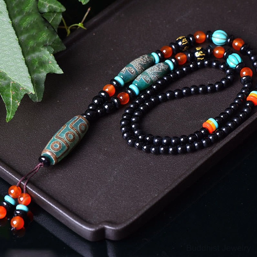 Buddhist nine-eye Dzi bead protection necklace detail view showing authentic dzi bead with traditional eye texture pattern and red-blue tassel pendant on dark background