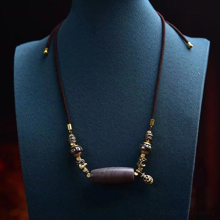 Full Nine-Eye Dzi Bead Om Mani Padme Hum Buddhist protection necklace displayed on blue jewelry mannequin with brown cord and gold accents