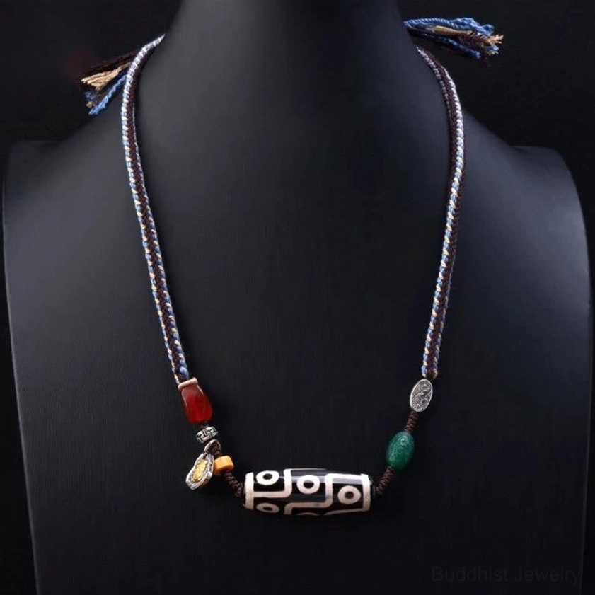 Nine-eye dzi bead Buddhist pendant necklace worn on mannequin, featuring protective agate bead with red and green stone spacers and minimalist Tibetan silver charm