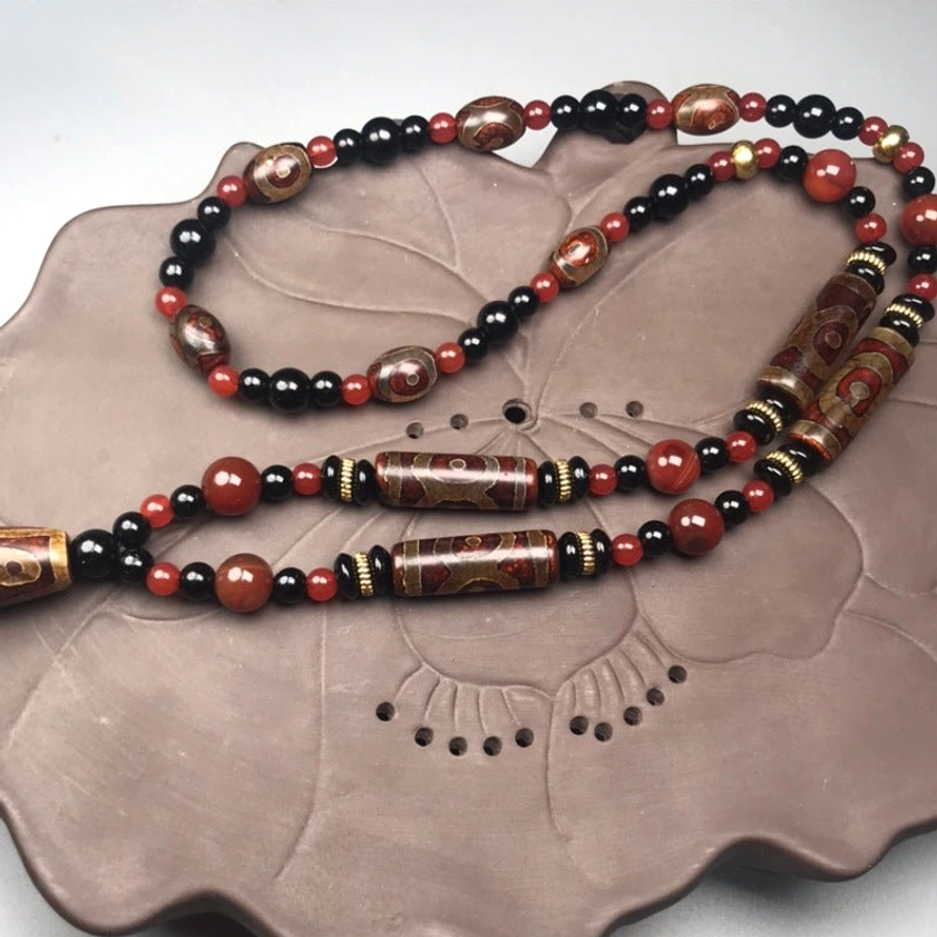 Multiple Nine-Eye Dzi Buddhist pendant necklaces displayed on decorative lotus-patterned ceramic tray, showcasing handcrafted beadwork in brown and reddish tones