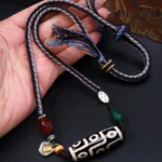 Nine-eye dzi bead Buddhist necklace held in palm, showing hand-painted natural agate bead with braided blue-brown rope and silver accent details